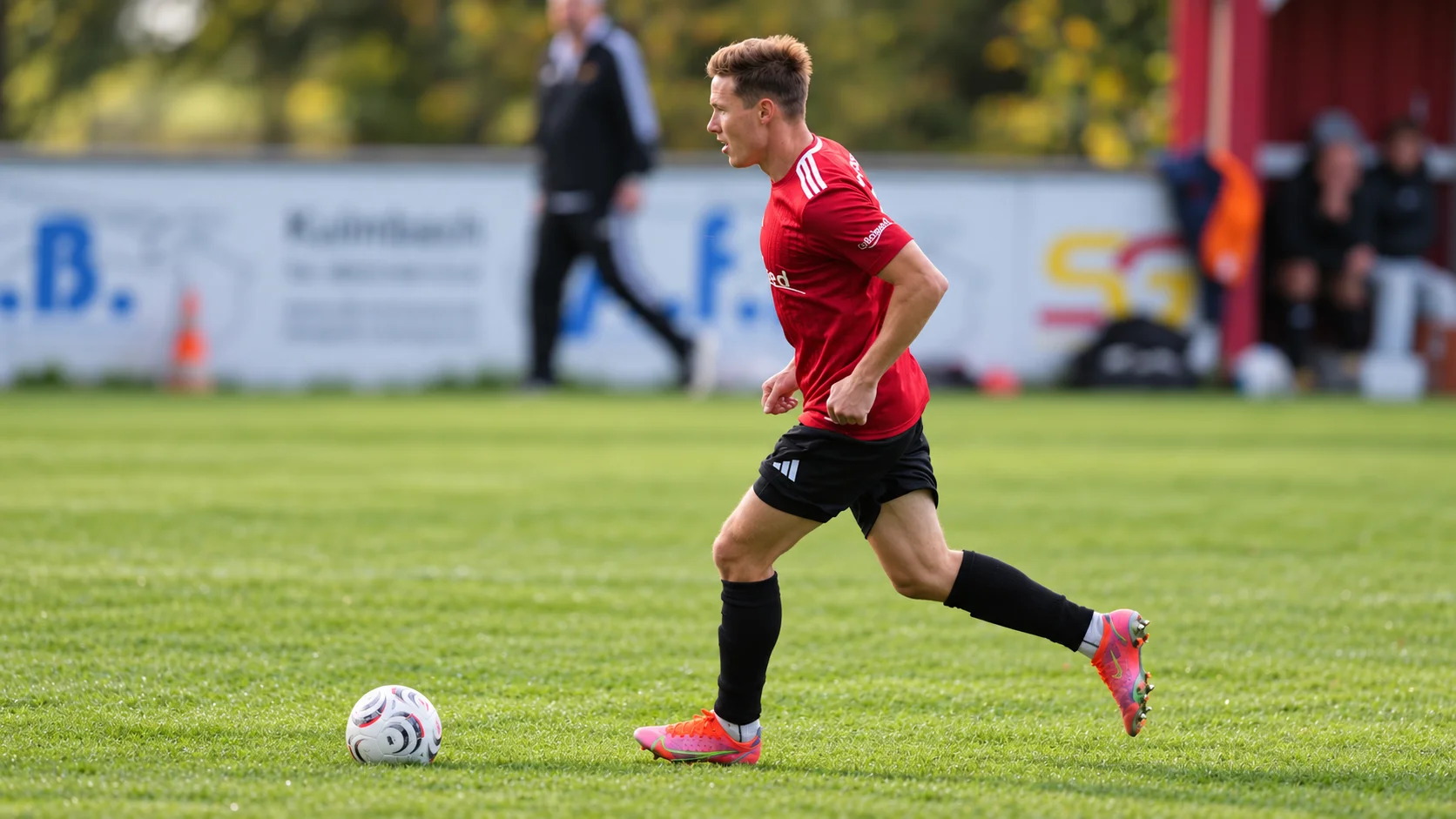 Fußballspieler im roten Colloimed-Trikot läuft mit dem Ball über den Rasen