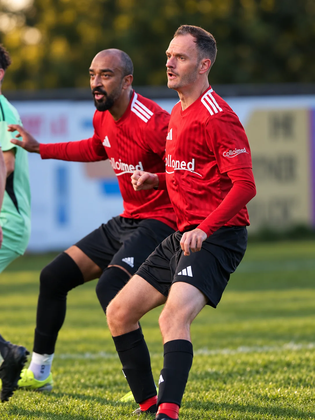 Spieler in roten Colloimed-Trikots und ein Gegenspieler in einer Spielszene