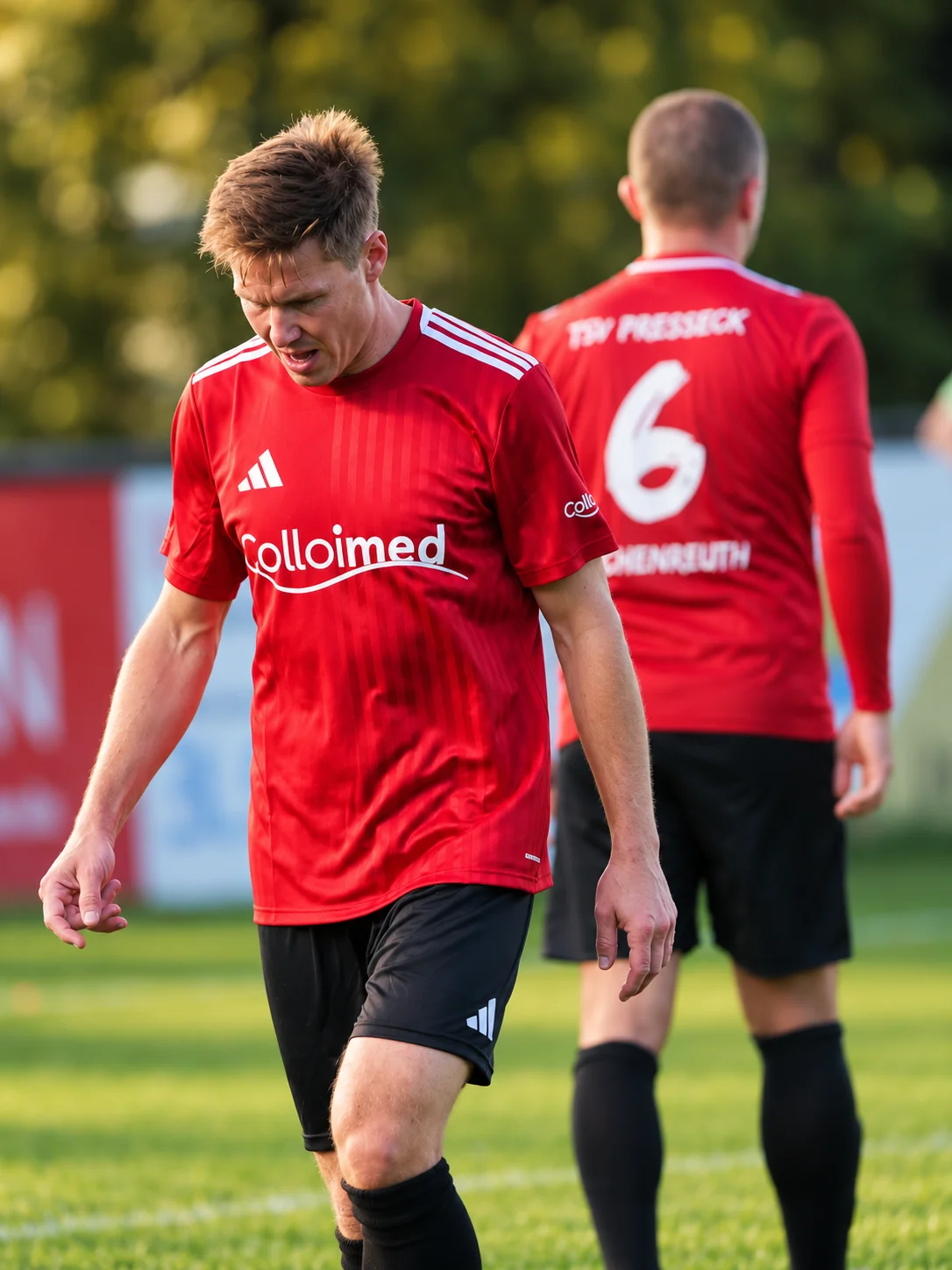 Zwei Fußballspieler in roten Colloimed-Trikots auf dem Rasen