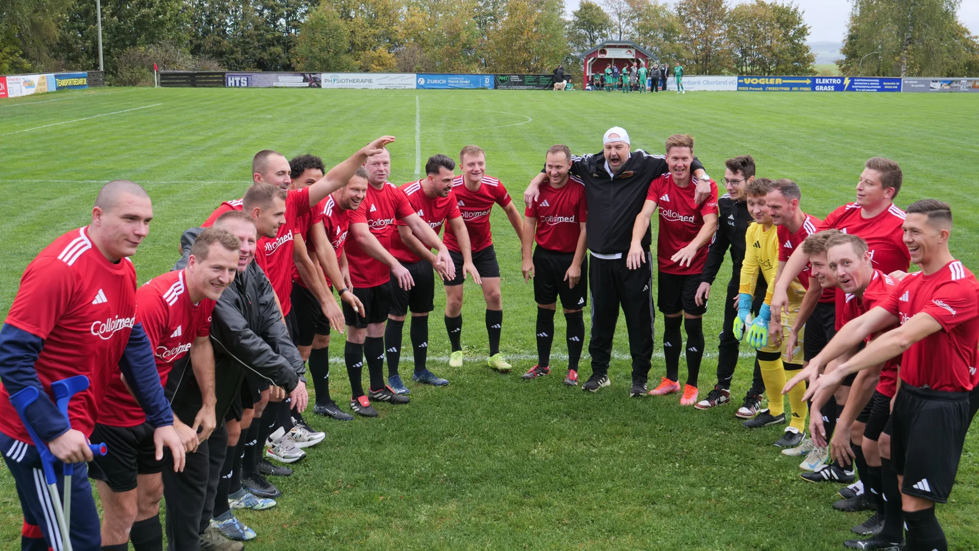 Mannschaft und Begleiter stehen auf dem Fußballplatz in einer gemeinsamen Runde