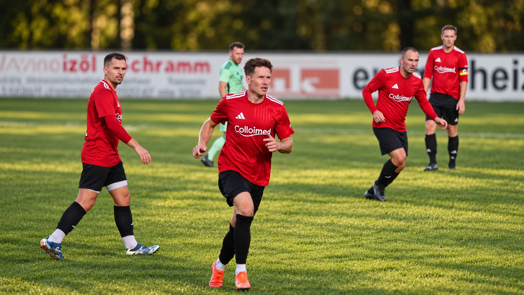 Drei Spieler in roten Colloimed-Trikots laufen über den Fußballplatz