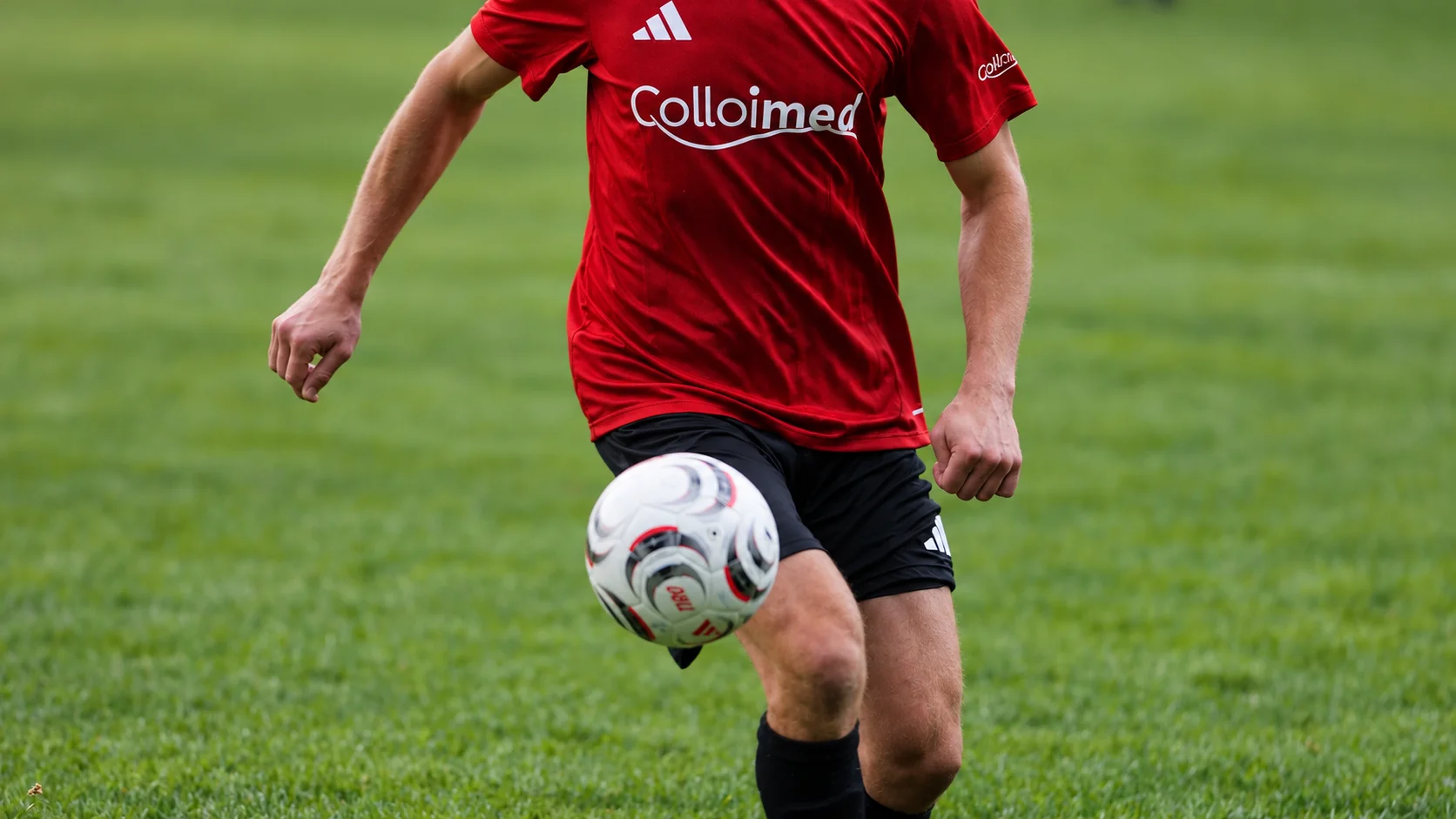 Detailaufnahme eines Fußballspielers im roten Colloimed-Trikot mit dem Ball vor dem Knie