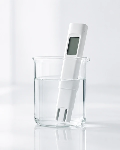 Becherglas mit Wasser und digitalem Leitwertmessgerät zur Prüfung der Wasserqualität